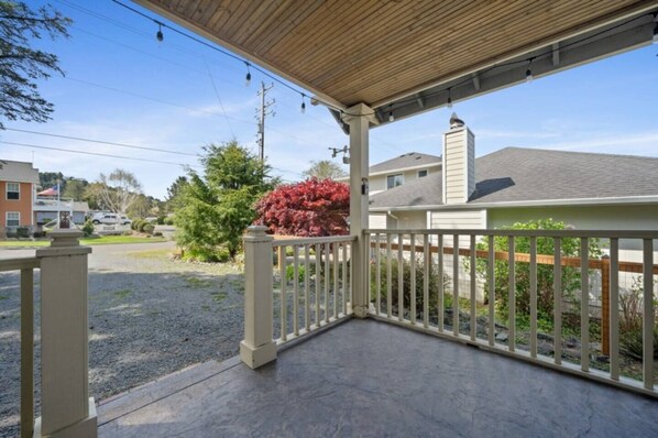 A covered porch with a view of residential houses and a gravel driveway.