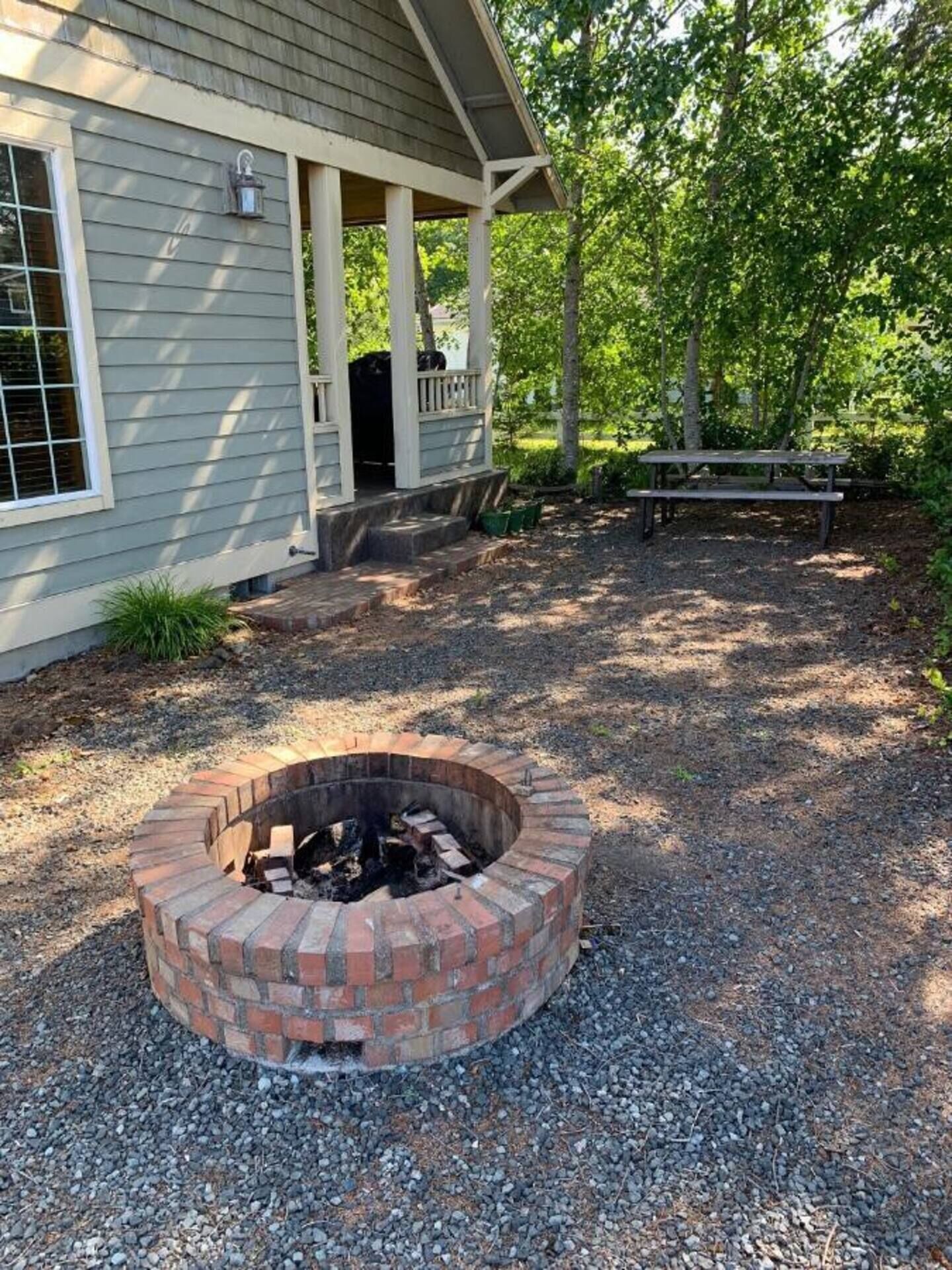 Ein Gebäude mit überdachter Veranda, Feuerstelle und Picknicktisch im Garten.