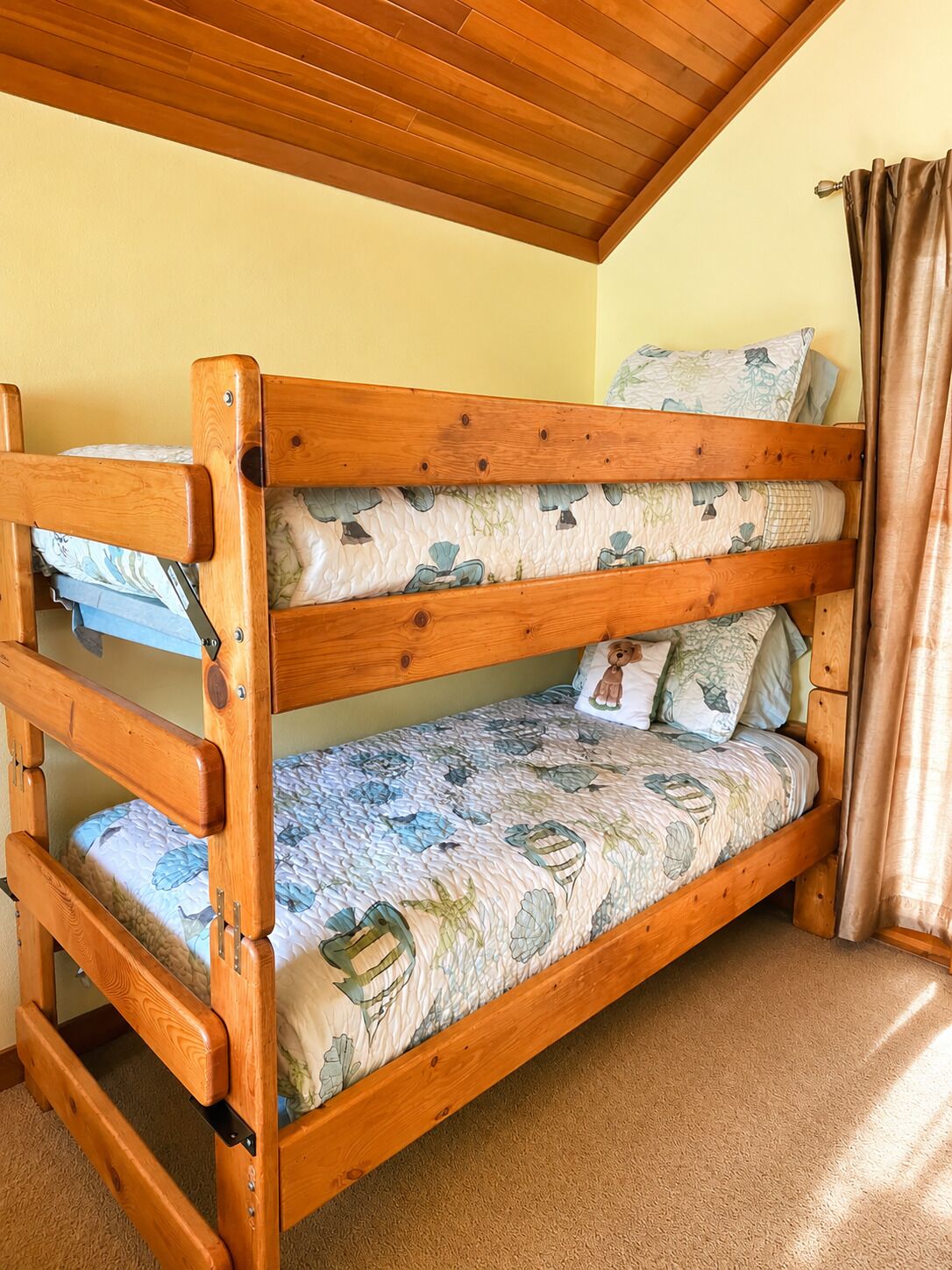 Un lit superposé avec un matelas à motifs floraux, une tête de lit en bois et un plafond avec des poutres apparentes.