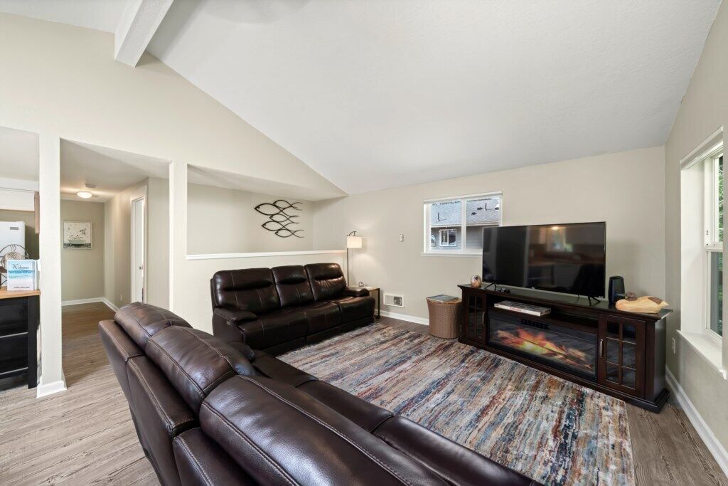 A living room with a brown leather sofa, a flat-screen TV, and a patterned rug.