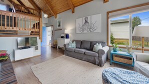 A cozy living room with a wooden ceiling, a grey sofa, a white cabinet, and artwork on the wall.