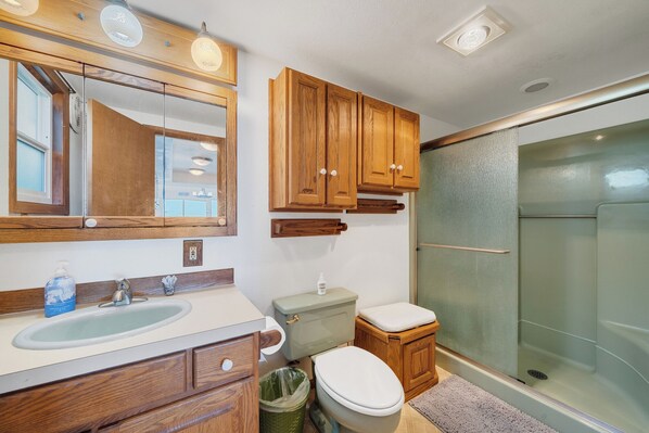 A bathroom with wooden cabinets, a sink, a toilet, and a glass shower enclosure.