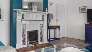 A room with a fireplace, a mirror, a television, and a blue table. - 3 bedroom accommodation in Corton, near Lowestoft (Corton, near Lowestoft)