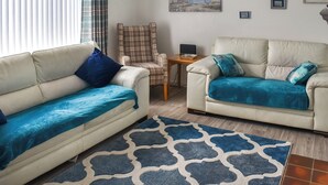 A living room with two sofas, a plaid armchair, a small table with a lamp, and artwork on the wall. - 3 bedroom accommodation in Corton, near Lowestoft (Corton, near Lowestoft)