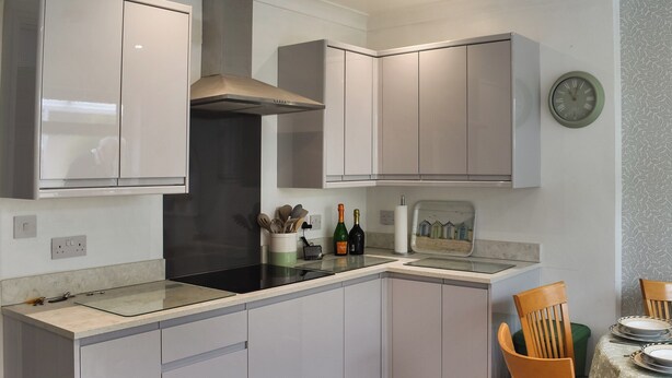 A modern kitchen with white cabinets, a black stove, and a dining area with wooden chairs and a table. - 3 bedroom accommodation in Corton, near Lowestoft (Corton, near Lowestoft)