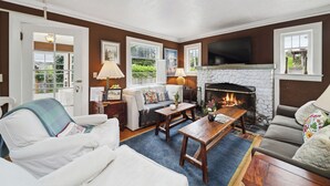 A living room with a fireplace, a sofa, a coffee table, and a television. - Susan’s Beach Cottage · Cozy Coastal Charm Just 1 Block from the Beach in the Heart of Manzanita (Manzanita)