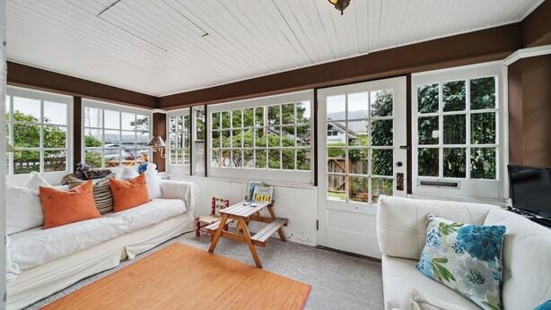 A sunlit room with white wooden walls, large windows, a white sofa, a wooden table, and a rug. - Susan’s Beach Cottage · Cozy Coastal Charm Just 1 Block from the Beach in the Heart of Manzanita (Manzanita)