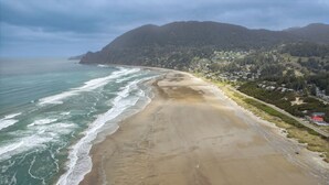 A coastal landscape with a sandy beach, ocean waves, and a forested hillside. - Susan’s Beach Cottage · Cozy Coastal Charm Just 1 Block from the Beach in the Heart of Manzanita (Manzanita)