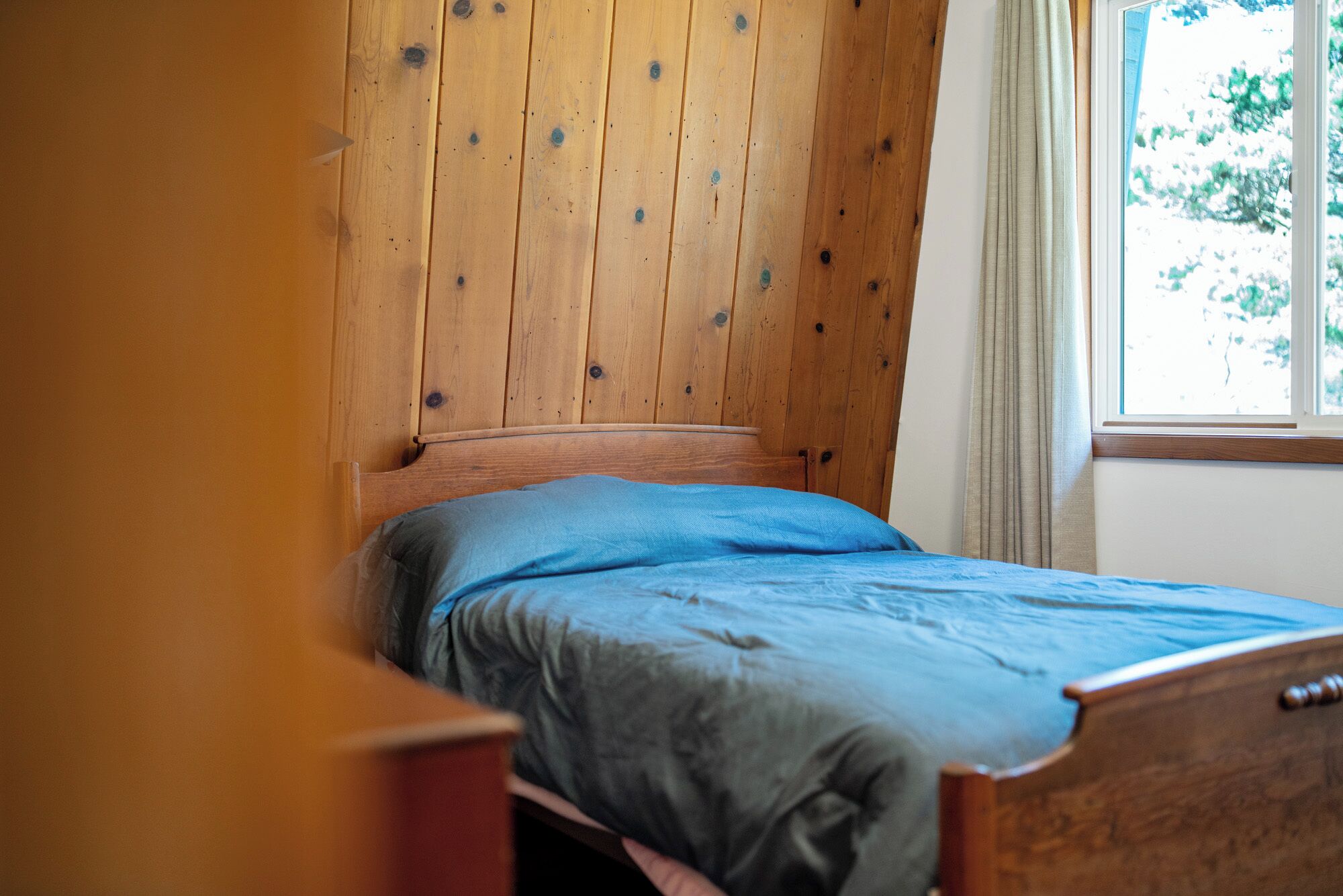 Una cama individual con cabecera de madera en una habitación con ventana y cortina.