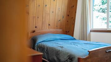 Una cama individual con cabecera de madera en una habitación con ventana y cortina.