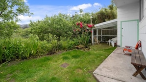Ein Haus mit überdachter Terrasse, Rasen und einem Garten mit verschiedenen Pflanzen und Blumen.