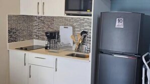 Eine kleine Küche mit weißen Schränken, einer Mikrowelle, einem Edelstahlkühlschrank und einer gefliesten Spritzschutzwand.