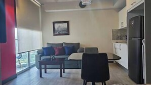 Ein modernes Wohnzimmer mit einer Couch, einem Couchtisch und einem Esstisch. Es gibt eine Küchenzeile mit einem Kühlschrank und Schränken.