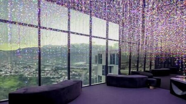Ein modernes Interieur mit großen Fenstern, einem violetten Teppich und Blick auf eine Stadtlandschaft.
