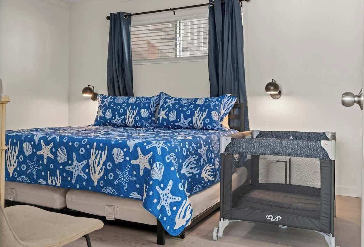 A bedroom with a bed, a small sofa, a window with curtains, and a baby playpen.