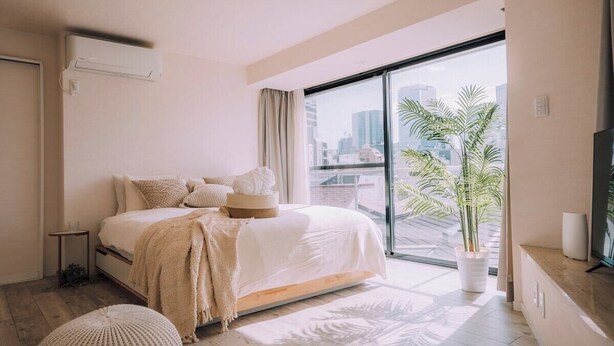 A modern bedroom with a large window, a bed with a white duvet, a bedside table, and a potted plant.