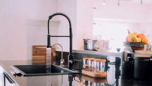 A modern kitchen with a black faucet, a glass pitcher, and a bowl of fruit on the counter.