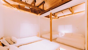 Une chambre avec deux lits, des poutres en bois au plafond et une fenêtre avec des stores.