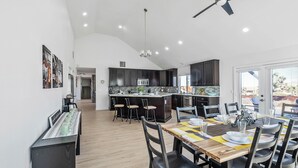 Une cuisine moderne avec des meubles de couleur sombre, un îlot central et un coin repas comprenant une table et des chaises en bois.