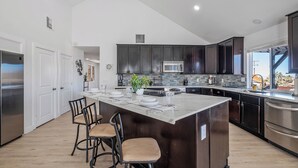 Une cuisine moderne avec des meubles de couleur sombre, des appareils en acier inoxydable et un grand îlot central doté de tabourets de bar.