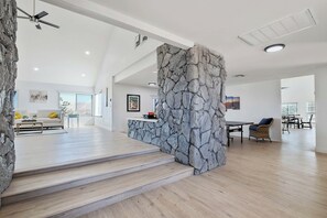 A spacious living area with a stone accent wall, a staircase, a dining area, and a sofa with yellow cushions. - Spacious and Relaxing Desert Retreat!! (Yucca Valley)