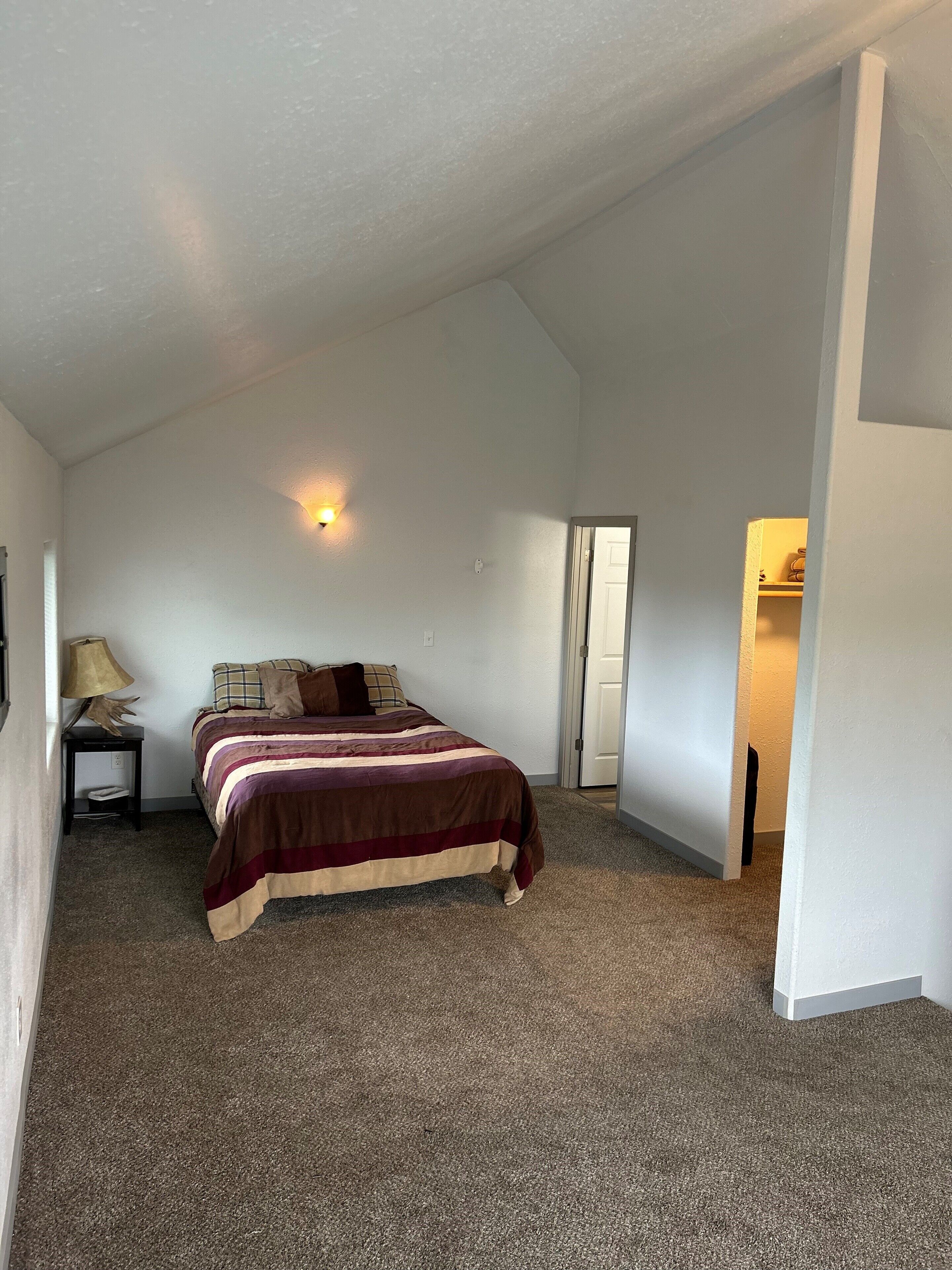 Un dormitorio con cama, mesita de noche, lámpara y puerta que da a otra habitación.