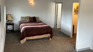 Un dormitorio con cama, mesita de noche, lámpara y puerta que da a otra habitación.