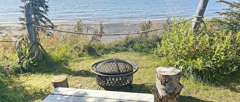 A picnic table and a metal grill in a grassy area with a view of the sea.
