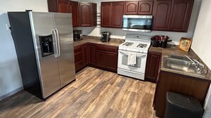 A kitchen with wooden cabinets, a stainless steel refrigerator, a microwave, a stove, and a sink.
