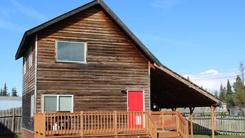 A two-story wooden cabin with a porch, a red door, and a window.