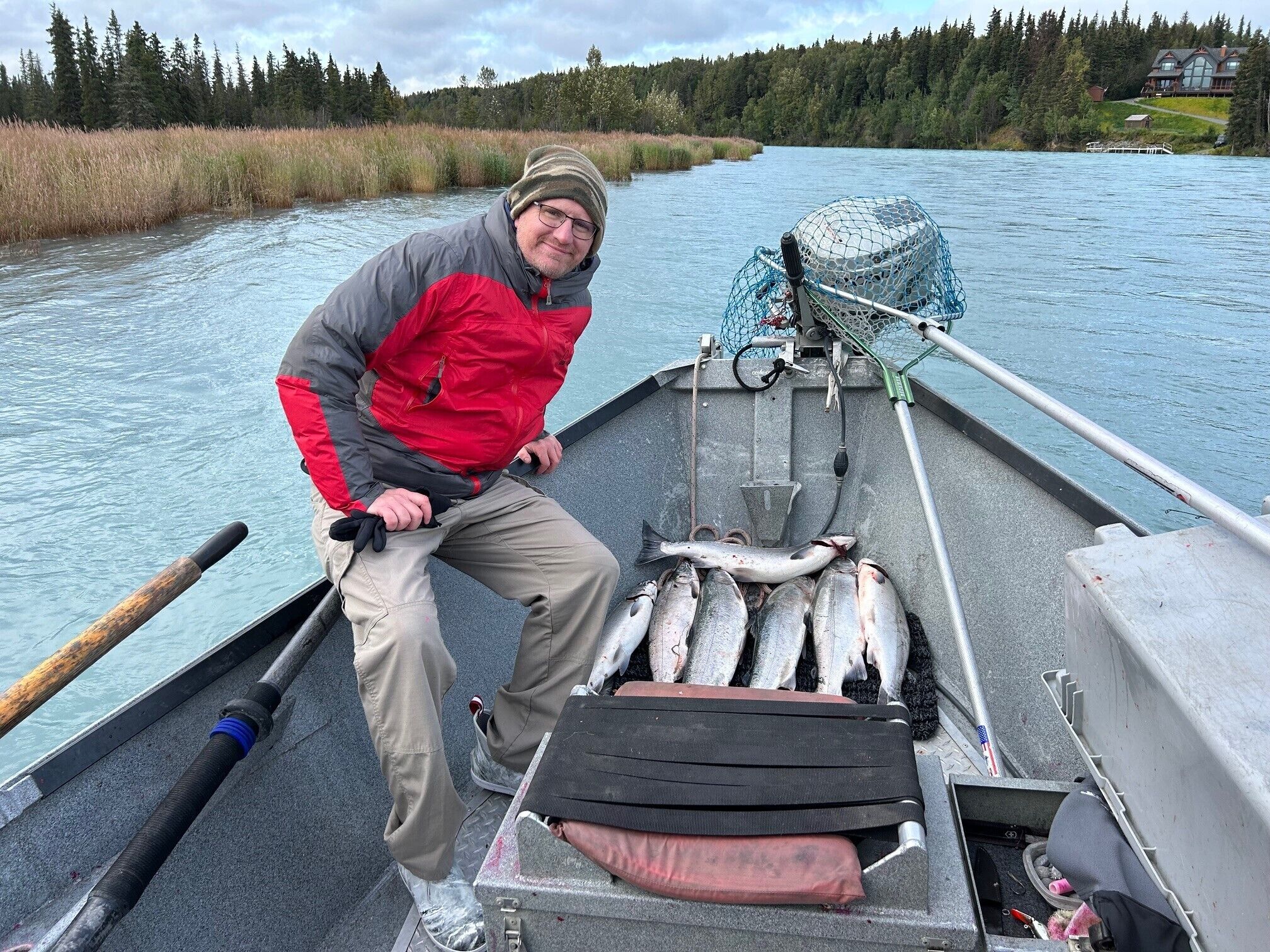 A boat with a person holding a fishing rod, several fish on the deck, and a net.