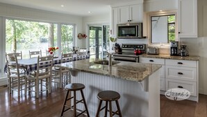 A modern kitchen with white cabinetry, a granite countertop, and a large island with stools. - 4bed, 4bath, South exp, prestigious area of Royal Muskoka Island w/road access (Minett)