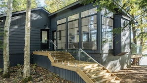 A modern house with a large window, a wooden staircase, and a black exterior. - 4bed, 4bath, South exp, prestigious area of Royal Muskoka Island w/road access (Minett)