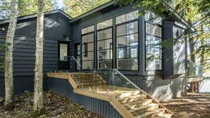A modern house with a large window, a wooden staircase, and a black exterior. - 4bed, 4bath, South exp, prestigious area of Royal Muskoka Island w/road access (Minett)