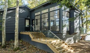 A modern house with a large window, a wooden staircase, and a black exterior. - 4bed, 4bath, South exp, prestigious area of Royal Muskoka Island w/road access (Minett)