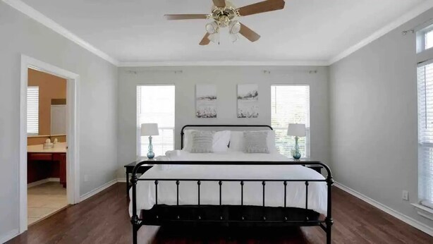 Une chambre à coucher avec un lit en métal noir, du linge de lit blanc, un ventilateur de plafond et deux lampes de chevet.