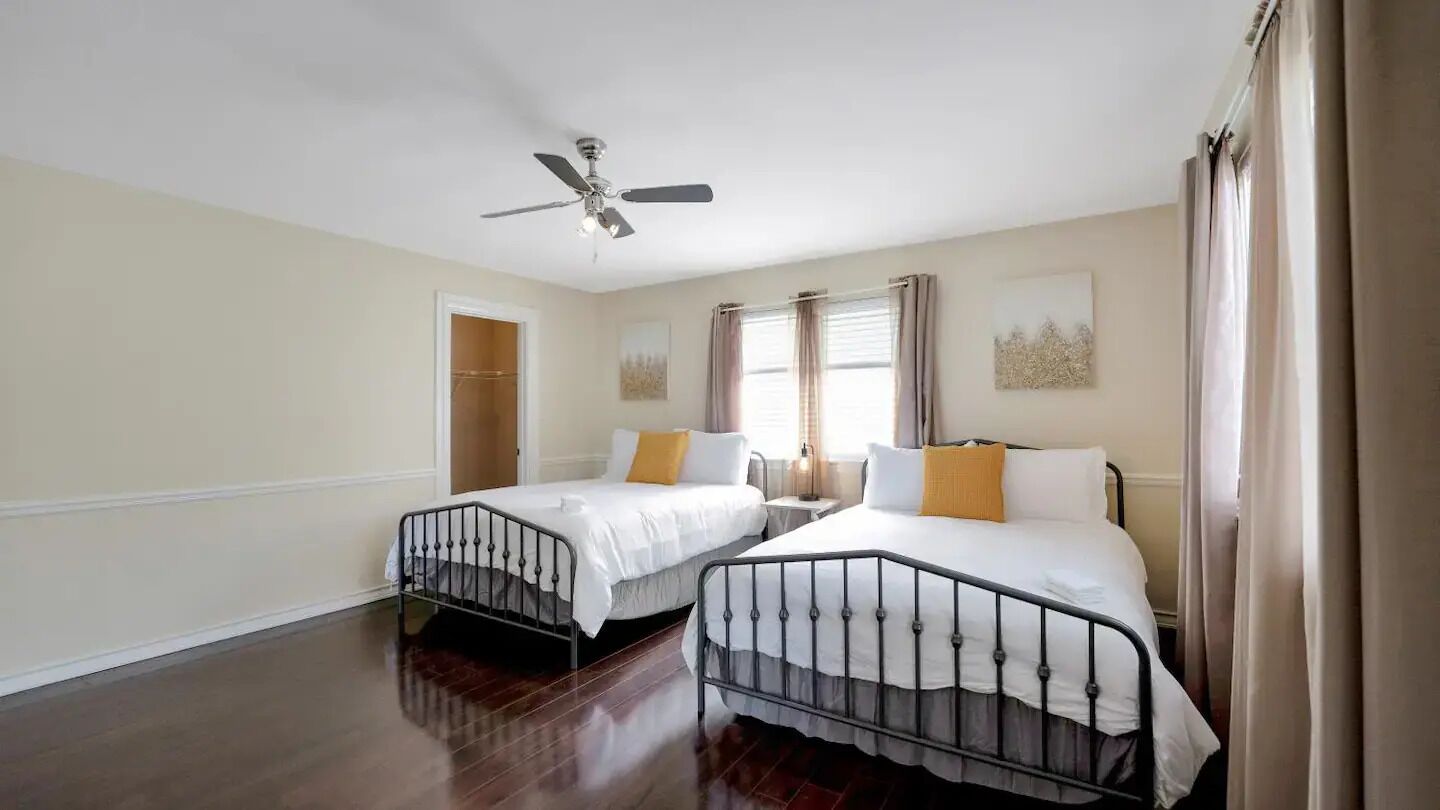 A hotel room with two beds, a ceiling fan, a window with curtains, and a door.