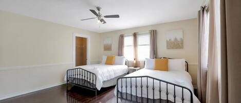 A hotel room with two beds, a ceiling fan, a window with curtains, and a door.