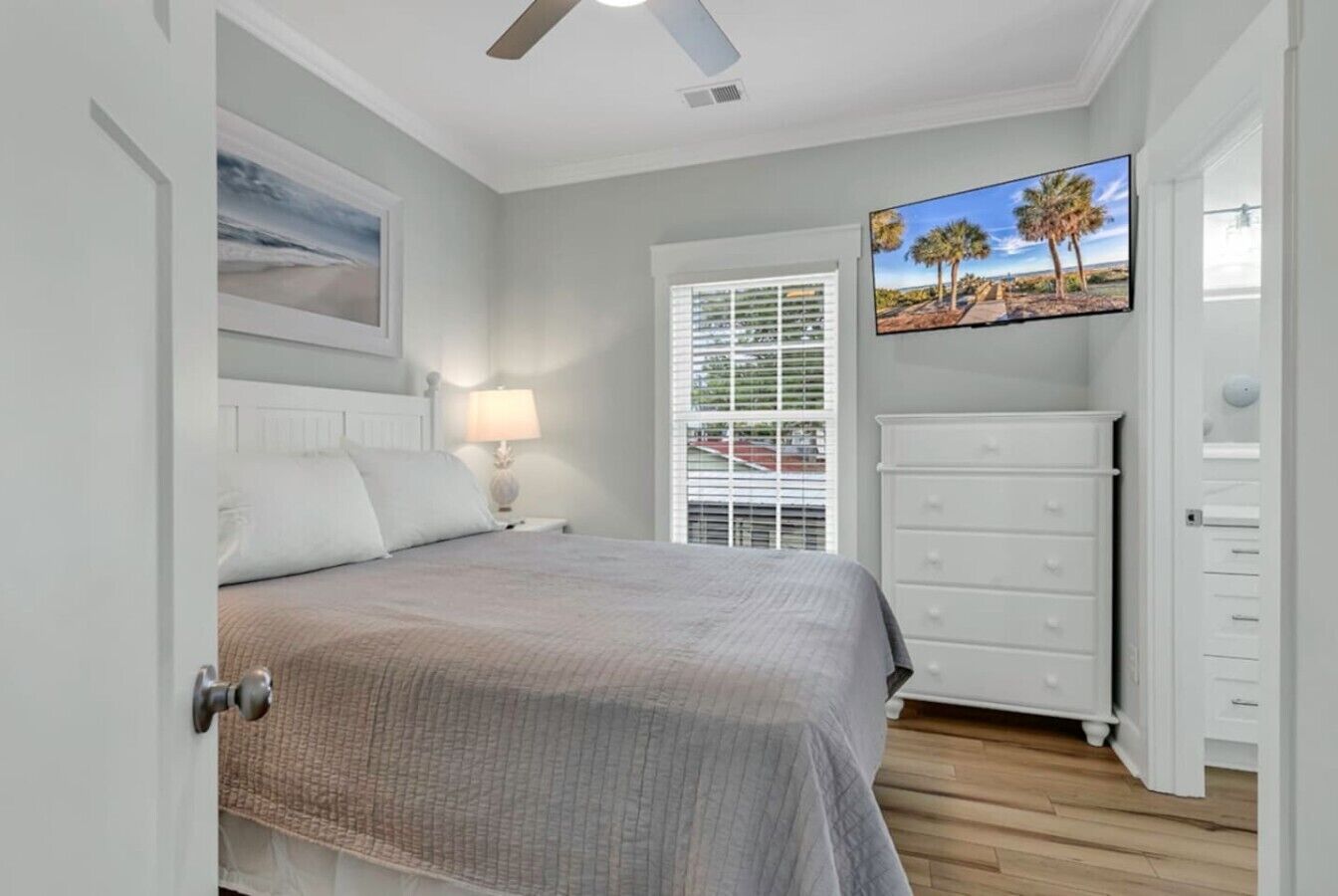 A bedroom with a bed, a nightstand, a dresser, a window with blinds, and a ceiling fan.