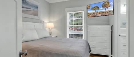 A bedroom with a bed, a nightstand, a dresser, a window with blinds, and a ceiling fan.