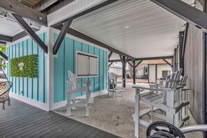 A covered outdoor seating area with white Adirondack chairs and a small table, a teal-colored wall with a window, and a green plant wall. - Ocean Lakes New Build, Steps to Beach and Balcony! (Myrtle Beach)