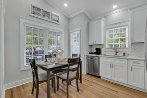 A modern kitchen with white cabinetry, a dining table with chairs, and a built-in dishwasher. - Ocean Lakes New Build, Steps to Beach and Balcony! (Myrtle Beach)