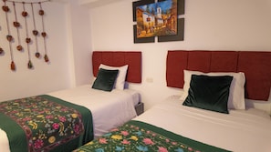A hotel room with two beds, each with red headboards and white bedding. There is a floral-patterned bedspread on the left bed. - Munay Cusco (Cusco)