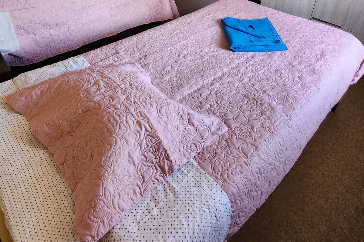 A room with two beds, a wardrobe, and a door leading to another room.