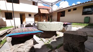 A courtyard with a stone table, outdoor seating, and a building with a tiled roof. - Munay Cusco (Cusco)