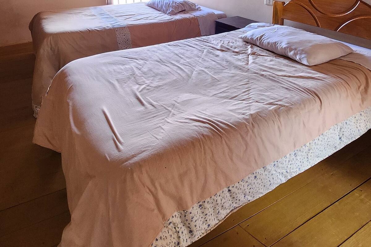 A room with two beds, wooden flooring, a sloped ceiling, and a window with natural light.
