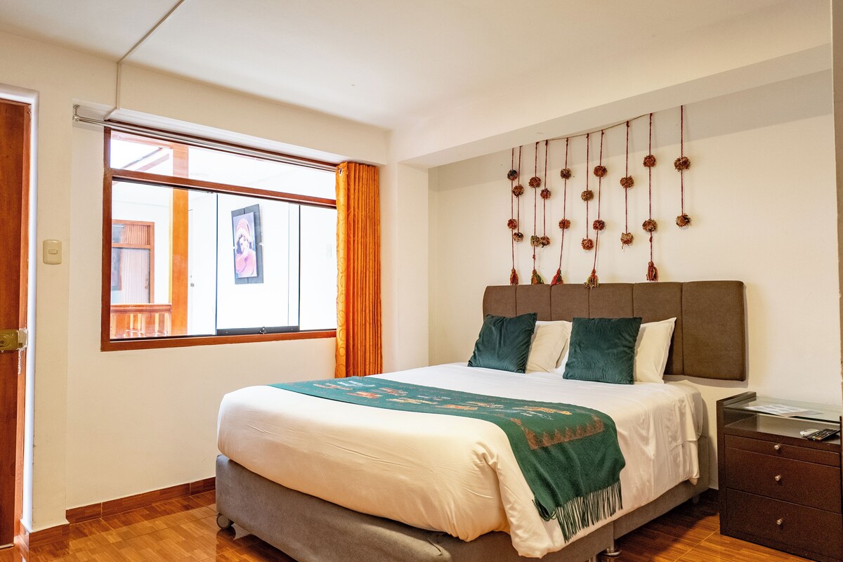 Een slaapkamer met een bed, nachtkastje, kapstok, raam met gordijnen en een wand met decoraties.