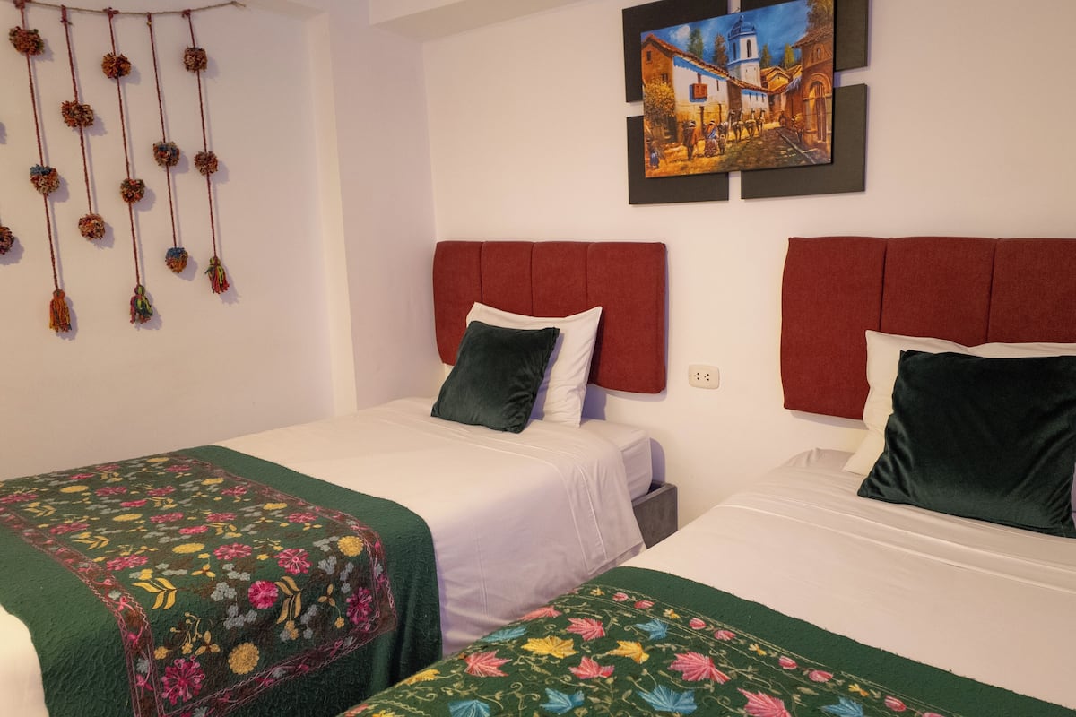 A hotel room with two beds, each with red headboards and white bedding. There is a floral-patterned bedspread on the left bed.