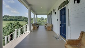 A covered porch with white columns, a blue door, and two wooden benches. - Spacious Rural Getaway in Lexington w/ Deck! (Lexington)
