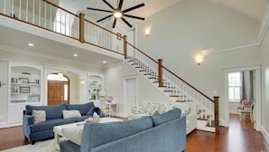 A spacious living room with a large blue sofa, a white coffee table, and a wooden staircase with a railing. - Spacious Rural Getaway in Lexington w/ Deck! (Lexington)